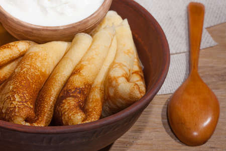 traditional oily food in vintage style: pancakes with sour cream in and a clay dish with a wooden spoon on an oak tableの写真素材