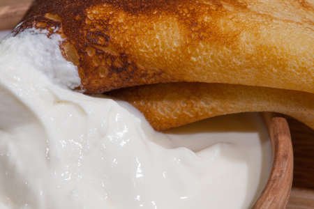 close-up of a pancake with sour cream in and a clay dish on an oak tableの写真素材