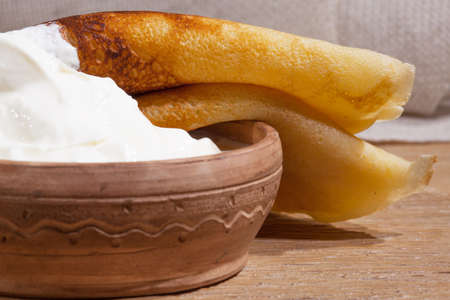 close-up of a pancake with sour cream in and a clay dish on an oak tableの写真素材