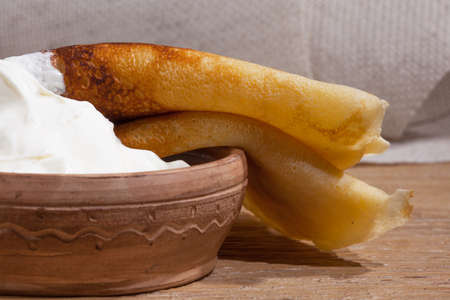 close-up of a pancake with sour cream in and a clay dish on an oak tableの写真素材