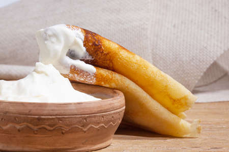 close-up of a pancake with sour cream in and a clay dish on an oak tableの写真素材