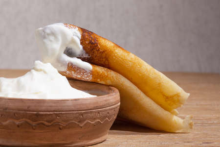 Close-up of a pancake with sour cream in and a clay dish on an oak tableの写真素材