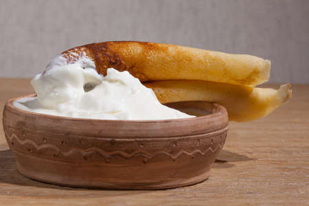 close-up of a pancake with sour cream in and a clay dish on an oak tableの写真素材