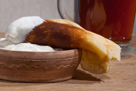 close-up of a pancake with sour cream in and a clay dish on an oak tableの写真素材