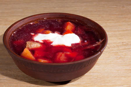 national Ukrainian food - borsch with sour cream with a wooden spoon in a clay plate on an oak tableの写真素材