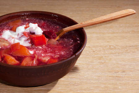 national Ukrainian food - borsch with sour cream with a wooden spoon in a clay plate on an oak tableの写真素材