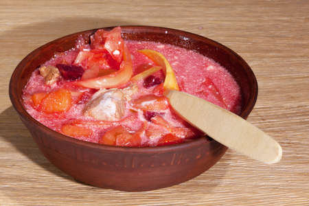 national Ukrainian food - borsch with sour cream with a wooden spoon in a clay plate on an oak tableの写真素材