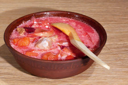 national Ukrainian food - borsch with sour cream with a wooden spoon in a clay plate on an oak tableの写真素材