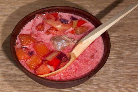 national Ukrainian food - borsch with sour cream with a wooden spoon in a clay plate on an oak tableの写真素材