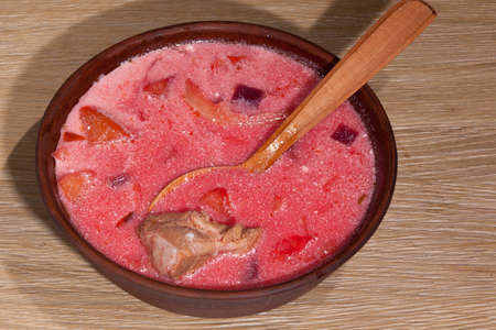 National Ukrainian food - borsch with sour cream with a wooden spoon in a clay plate on an oak tableの写真素材