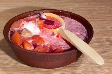 national Ukrainian food - borsch with sour cream with a wooden spoon in a clay plate on an oak tableの写真素材