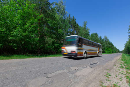 shuttle bus rides a bad country road to the edge of a coniferous forest A bright summer sunny dayの写真素材