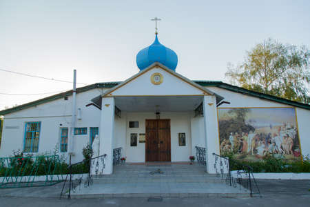 Christian church with a golden cross and a blue-blue dome in the village with a fresco on the wall early morning sunの写真素材