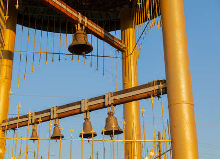 Christian belltower with wooden crossbar bronze bells golden cross and dome in the village early morning sun view from belowの写真素材