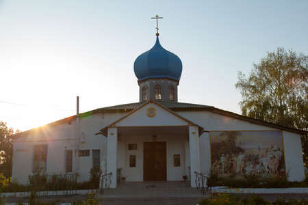 Christian church with a golden cross and a blue-blue dome in the village with a fresco on the wall early morning sunの写真素材