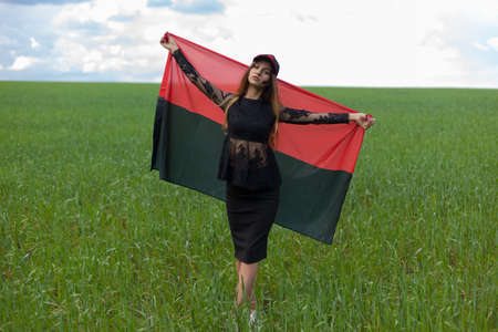 young beautiful ukrainian girl with an excellent figure in a black short dress holds a national Ukrainian red black flagの写真素材