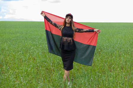 young beautiful ukrainian girl with an excellent figure in a black short dress holds a national Ukrainian red black flagの写真素材