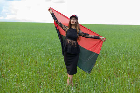 young beautiful ukrainian girl with an excellent figure in a black short dress holds a national Ukrainian red black flagの写真素材