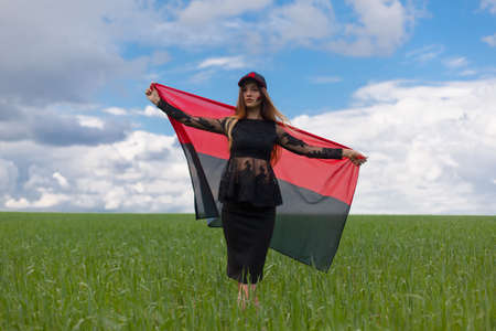 young beautiful ukrainian girl with an excellent figure in a black short dress holds a national Ukrainian red black flagの写真素材
