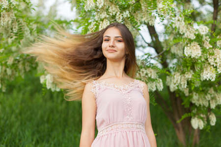 sexual girl has dissolved long hair sunny in the afternoon opposite blossoming white acaciaの写真素材