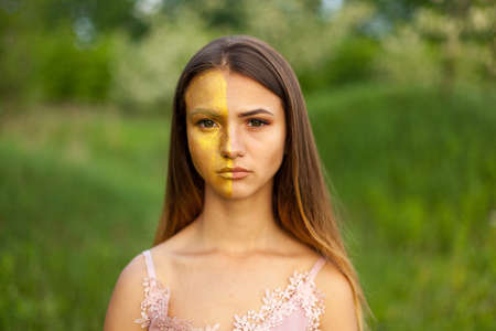 close-up portrait of a beautiful young girl in around white acacia in the spring half face golden make-upの写真素材