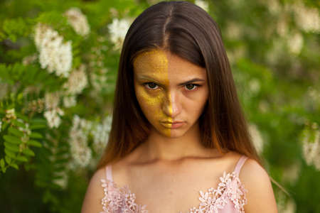 close-up portrait of a beautiful young girl in around white acacia in the spring half face golden make-upの写真素材