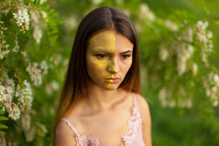 close-up portrait of a beautiful young girl in around white acacia in the spring half face golden make-upの写真素材