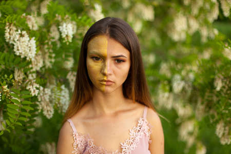close-up portrait of a beautiful young girl in around white acacia in the spring half face golden make-upの写真素材