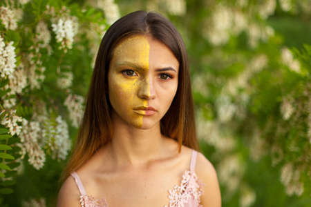close-up portrait of a beautiful young girl in around white acacia in the spring half face golden make-upの写真素材