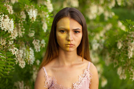 close-up portrait of a beautiful young girl in around white acacia in the spring half face golden make-upの写真素材