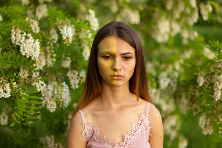 close-up portrait of a beautiful young girl in around white acacia in the spring half face golden make-upの写真素材
