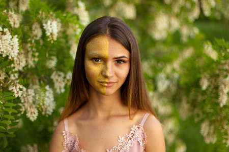 close-up portrait of a beautiful young girl in around white acacia in the spring half face golden make-upの写真素材