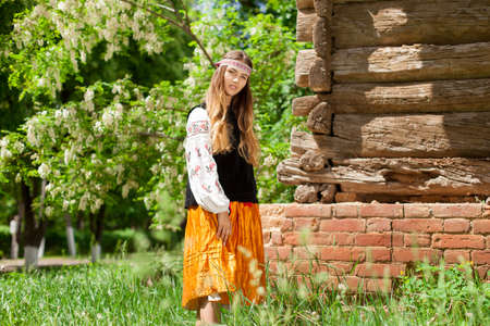 Beautiful slender Ukrainian woman in embroidery on the background of a wooden frame of a barn in the villageの写真素材
