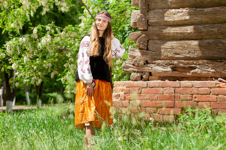 Beautiful slender Ukrainian woman in embroidery on the background of a wooden frame of a barn in the villageの写真素材