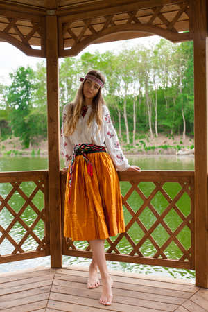 Beautiful slender Ukrainian in embroidery in windy weather enjoys a rest on the lake on a summer sunny dayの写真素材