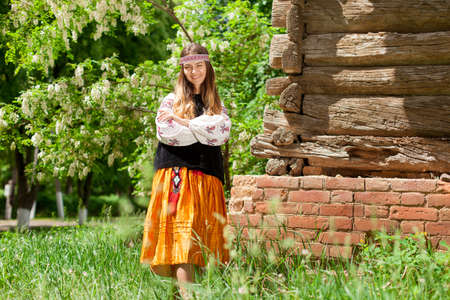 Beautiful slender Ukrainian woman in embroidery on the background of a wooden frame of a barn in the villageの写真素材
