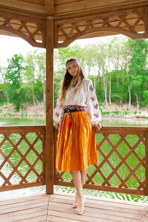 Beautiful slender Ukrainian in embroidery in windy weather enjoys a rest on the lake on a summer sunny dayの写真素材