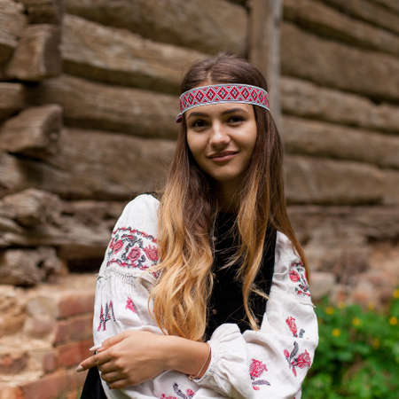 Beautiful slender Ukrainian woman in embroidery on the background of a wooden frame of a barn in the villageの写真素材