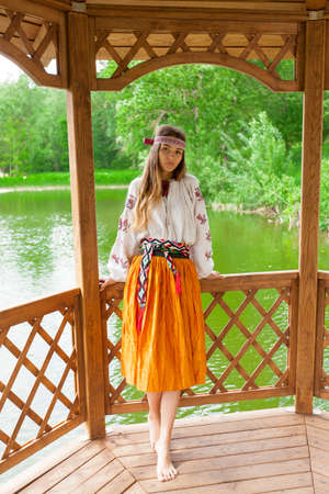 Beautiful slender Ukrainian in embroidery in windy weather enjoys a rest on the lake on a summer sunny dayの写真素材