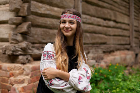 Beautiful slender Ukrainian woman in embroidery on the background of a wooden frame of a barn in the villageの写真素材