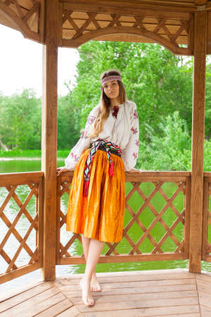 Beautiful Ukrainian woman dressed in embroidery in a wooden summer altanka on a lakeの写真素材