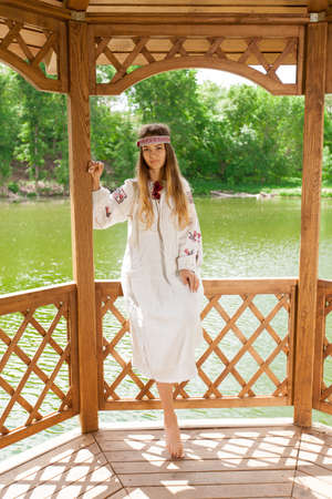 Beautiful slender Ukrainian in embroidery in windy weather enjoys a rest on the lake on a summer sunny dayの写真素材