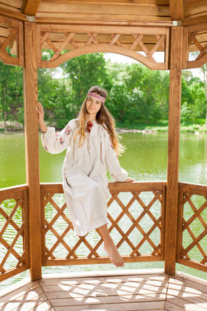 Beautiful Ukrainian woman dressed in embroidery in a wooden summer altanka on a lakeの写真素材
