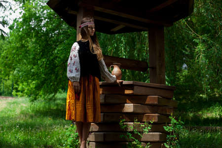 Beautiful Ukrainian woman is wearing embroidery near a wooden wellの写真素材