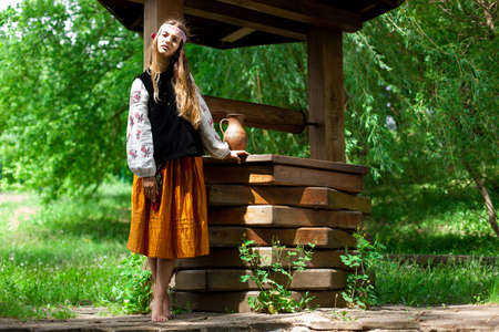 Beautiful Ukrainian woman is wearing embroidery near a wooden wellの写真素材