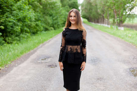 Beautiful slender Ukrainian woman in stylish black clothes on the asphalt old roadの写真素材