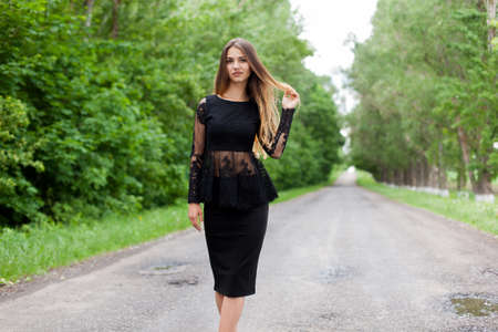 Beautiful slender Ukrainian woman in stylish black clothes on the asphalt old roadの写真素材