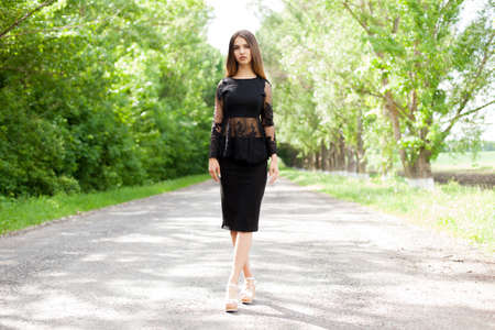 Beautiful slender Ukrainian woman in stylish black clothes on the asphalt old roadの写真素材
