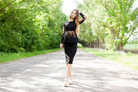 Beautiful slender Ukrainian woman in stylish black clothes on the asphalt old roadの写真素材