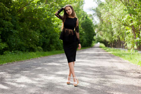Beautiful slender Ukrainian woman in stylish black clothes on the asphalt old roadの写真素材